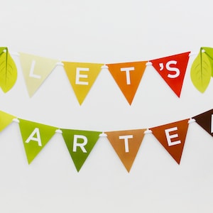May include: A colorful triangle banner with the words "Let's Party" and green leaves on either end.
