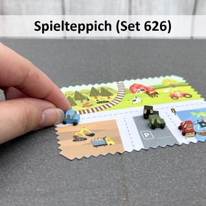 Könnte beinhalten: Ein farbenfroher Spielteppich mit Straßen- und Landschaftsdesign, mit Miniaturautos, Lastwagen und Baufahrzeugen. Der Text "Spielteppich (Set 626)" steht oben. Ein blaues Auto wird auf die Matte gesetzt.