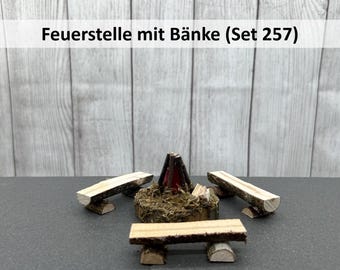Può includere: Un camino in miniatura di legno con tre panche in legno. Il camino è in legno marrone e ha un camino rosso e nero. Le panche sono in legno marrone chiaro. Il set è etichettato "Feuerstelle mit Bänke (Set 257)".