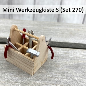 Könnte beinhalten: Eine kleine Holzkiste mit rotem Griff und einem Satz Miniaturwerkzeuge, darunter Zangen, ein Schraubenschlüssel, ein Hammer und ein Schraubendreher. Die Werkzeugkiste ist mit "Mini Werkzeugkiste S (Set 270)" beschriftet.