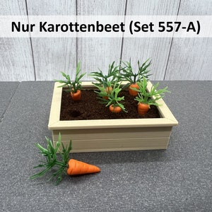 Könnte beinhalten: Ein hölzerner Pflanzkasten gefüllt mit Erde und fünf kleinen Karottenpflanzen. Die Karotten sind orange und die Pflanzen haben grüne Blätter. Der Pflanzkasten steht auf einer grauen Oberfläche. Der Text "Nur Karottenbeet (Set 557-A)" ist auf einem weißen Banner über dem Pflanzkasten gedruckt.