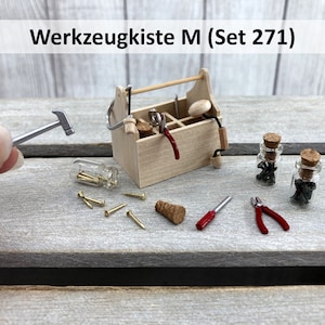 Könnte beinhalten: Eine Miniatur-Holzkiste mit Griff, gefüllt mit Miniaturwerkzeugen, darunter Hammer, Säge, Zange und Schraubendreher. Außerdem gibt es zwei kleine Glasbehälter gefüllt mit Miniatur-Nägeln und Schrauben. Die Werkzeugkiste ist mit "Werkzeugkiste M (Set 271)" beschriftet.