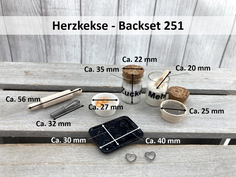 May include: A miniature baking set with a rolling pin, a whisk, a bowl of yellow dough, a baking sheet, a sifter, and two jars labelled "Zucker" and "Mehl". The set is labelled "Herzkekse - Backset 251".