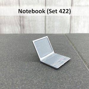 Könnte beinhalten: Ein silberner Laptop mit geschlossenem Deckel. Der Laptop befindet sich auf einer grauen Oberfläche. Der Text "Notebook (Set 422)" ist über dem Laptop sichtbar.