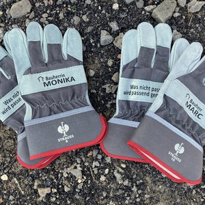 Könnte beinhalten: Zwei Paar graue Arbeitshandschuhe mit rotem Besatz. Die Handschuhe haben den Text "Was nicht passt wird passend gemacht" und "Bauherr MARC" aufgedruckt. Die Handschuhe haben auch das Strauss-Logo aufgedruckt.
