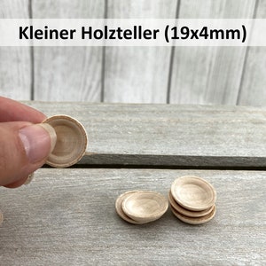 Könnte beinhalten: Vier kleine Holzschalen, eine wird in der Hand gehalten, die anderen liegen auf einer Holzoberfläche. Die Schalen haben einen Durchmesser von 19 mm und eine Höhe von 4 mm. "Kleiner Holzteller (19x4mm)" steht in der oberen linken Ecke des Bildes.