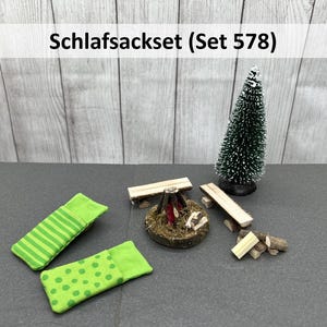 Könnte beinhalten: Ein Miniatur-Camping-Set mit zwei grünen Schlafsäcken, einem kleinen Lagerfeuer, zwei Holzbänken und einem Holzstapel. Das Set ist mit "Schlafackset (Set 578)" beschriftet.