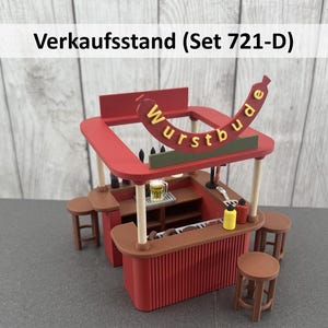 Könnte beinhalten: Ein Miniaturmodell eines roten und braunen Imbissstandes mit dem Text "Wurstbude" in Gelb. Der Stand hat eine Theke, Hocker und ein kleines Bierglas. Der Text "Verkaufsstand (Set 721-D)" befindet sich über dem Stand.