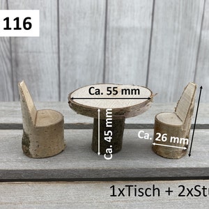 May include: A set of miniature wooden furniture, including a table and two chairs, made from natural birch wood. The table is approximately 5.5 cm in diameter and 4.5 cm tall. The chairs are approximately 2.6 cm wide and 5 cm tall. The set is labelled "Set 116" and "1xTisch + 2xSt&uuml;hle".