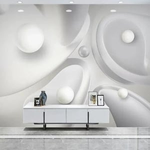 May include: A modern white and gray abstract wall mural with 3D spherical and curved design elements. The mural features various sizes of white spheres and flowing, organic shapes, creating a sense of depth and movement. A white cabinet with decor is below the mural.