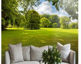 May include: A white couch with three pillows sits in front of a photo mural depicting a sunny green meadow with trees in the background.