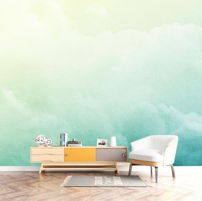 K&ouml;nnte beinhalten: Eine helle Holz-Medienkonsole mit zwei Schubladen und einer gelben und grauen T&uuml;r. Die Konsole steht vor einer Wand mit einem Aquarell-Hintergrund aus gr&uuml;nen und blauen Wolken.