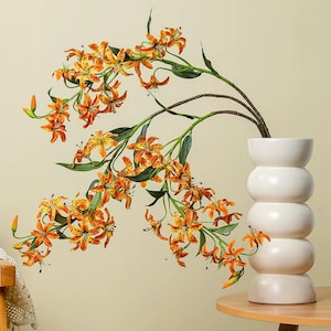 Può includere: Un vaso bianco impilato in ceramica contiene un ramo di gigli tigrati arancioni e gialli con foglie verdi. Il vaso è appoggiato su un tavolo rotondo di legno. I gigli hanno macchie scure e sono in piena fioritura.