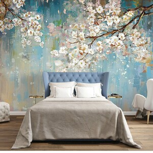 Op de afbeelding: Een slaapkamer met een bed met een blauwe hoofdeinde, witte beddengoed en een witte stoel. De muur achter het bed is een muurschildering met een blauwe achtergrond en witte bloemen.