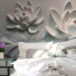 K&ouml;nnte beinhalten: Wei&szlig;e 3D-Lotusblumen-Wandkunst mit einem wei&szlig;en Bett mit wei&szlig;en Bettw&auml;sche und Kissen davor. Eine kleine Topfpflanze mit lila Bl&uuml;ten steht auf einer kleinen Holzkiste.