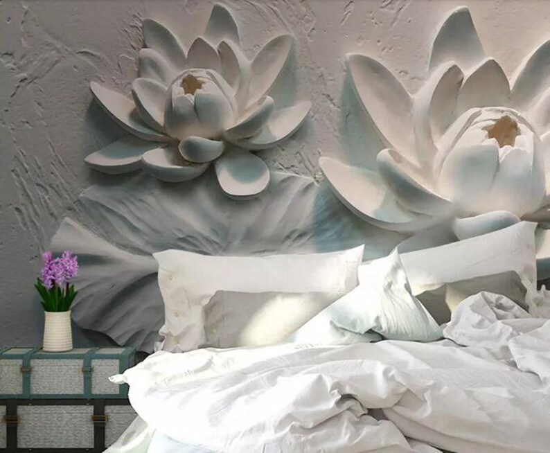 K&ouml;nnte beinhalten: Wei&szlig;e 3D-Lotusblumen-Wandkunst mit einem wei&szlig;en Bett mit wei&szlig;en Bettw&auml;sche und Kissen davor. Eine kleine Topfpflanze mit lila Bl&uuml;ten steht auf einer kleinen Holzkiste.