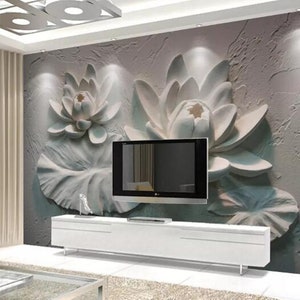K&ouml;nnte beinhalten: Eine wei&szlig;e 3D-Wandmalerei mit einer gro&szlig;en, stilisierten Lotusblume auf einem strukturierten, grauen Hintergrund. Ein Flachbildfernseher ist unterhalb der Wandmalerei an der Wand montiert.