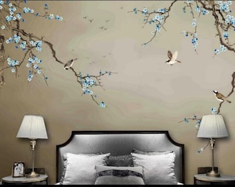May include: A bedroom interior with a gray headboard bed, two white pillows, and a patterned pillow. Two lamps with white lampshades are on nightstands on either side of the bed. The wall behind the bed features a mural of a brown tree branch with blue flowers and three birds.