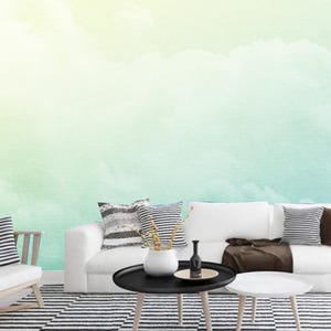 K&ouml;nnte beinhalten: Ein wei&szlig;es Sofa mit braunen Kissen und einer schwarz-wei&szlig; gestreiften Decke. Das Sofa steht vor einer Wand mit einem Aquarellbild von Wolken in Gr&uuml;n- und Gelbt&ouml;nen.