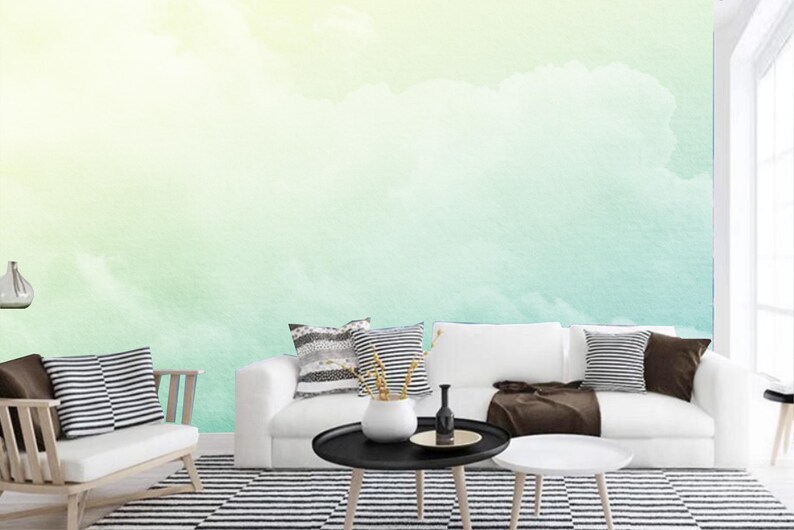 K&ouml;nnte beinhalten: Ein wei&szlig;es Sofa mit braunen Kissen und einer schwarz-wei&szlig; gestreiften Decke. Das Sofa steht vor einer Wand mit einem Aquarellbild von Wolken in Gr&uuml;n- und Gelbt&ouml;nen.