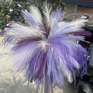 May include: A bouquet of decorative feathers in shades of purple, lavender, and white. The arrangement features long, fluffy plumes, creating a full and textured appearance. Ideal for home decor or crafting projects.