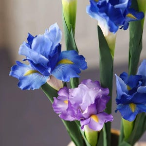May include: Close-up of artificial iris flowers in shades of blue and purple. The petals have yellow accents and are arranged around green stems. The flowers are in full bloom, showcasing their intricate details.
