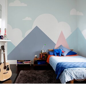 May include: A bedroom with a blue, pink, and white mountain mural on the wall. A bed with a blue and white checkered blanket and a blue stuffed animal is in the room. There is a guitar leaning against the wall and a wooden side table with books on it.