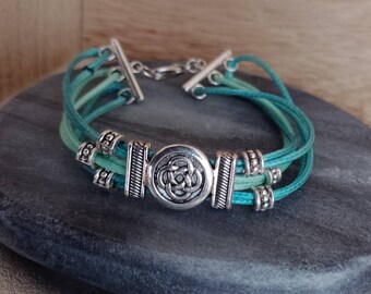Bracelet with metal sliding bead knot symbol and polyester straps in turquoise tones