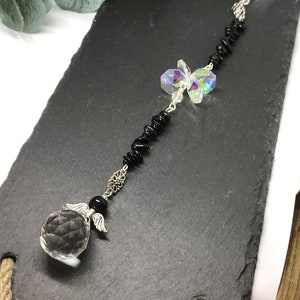 May include: A crystal suncatcher with black beads and a butterfly charm. The suncatcher has a clear crystal ball with silver angel wings at the bottom.