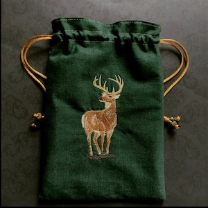 May include: A green drawstring bag with a gold cord. The bag features an embroidered image of a brown deer with antlers.