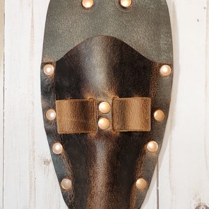 May include: A brown leather tool holder with a brown leather strap and metal rivets. The holder has a dark brown finish and is designed to hold tools.