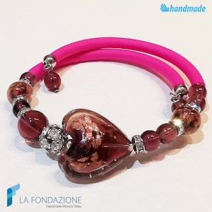 May include: A pink elastic bracelet with a heart-shaped Murano glass charm and purple glass beads. The charm has a gold leaf design.