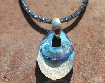 May include: A blue and gold glass pendant necklace with a sparkly black chain. The pendant is shaped like a teardrop and has a swirl design.