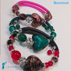 May include: Three bracelets with colorful glass hearts and beads. The bracelets are made with black, teal, and pink elastic. The hearts are in shades of green, brown, and purple. The beads are red, green, and purple.