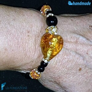 Puede incluir: Un brazalete hecho a mano con un gran dije de coraz&oacute;n de &aacute;mbar, cuentas negras y detalles de diamantes de imitaci&oacute;n transparentes.
