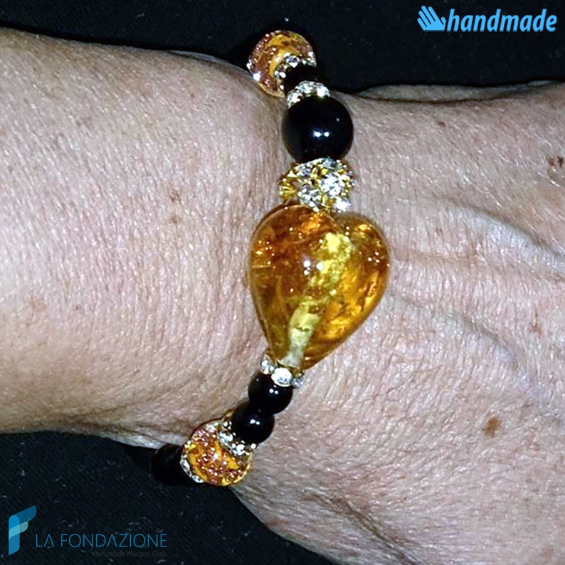 Puede incluir: Un brazalete hecho a mano con un gran dije de coraz&oacute;n de &aacute;mbar, cuentas negras y detalles de diamantes de imitaci&oacute;n transparentes.