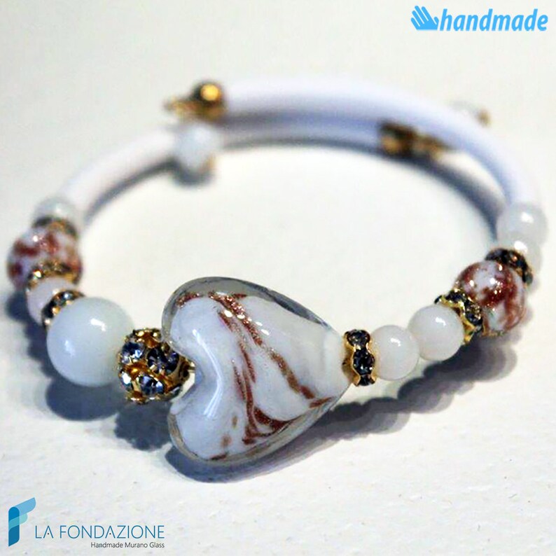 May include: White bracelet with a heart-shaped Murano glass bead, white and gold beads, and clear rhinestones. The bracelet is handmade and features the text "LA FONDAZIONE Handmade Murano Glass".