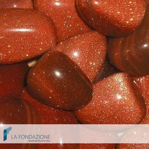 May include: Close-up of a group of red, sparkly, tumbled stones. The stones have a shiny, metallic finish and are arranged in a random pattern.