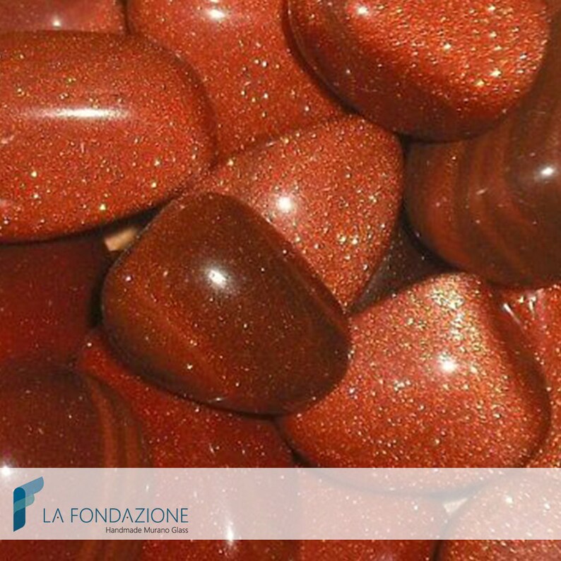 May include: Close-up of a group of red, sparkly, tumbled stones. The stones have a shiny, metallic finish and are arranged in a random pattern.