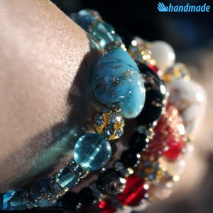 May include: A stack of colorful bracelets with turquoise, black, white, and red beads. The bracelets are adorned with gold accents and clear rhinestones. The bracelets are handmade.