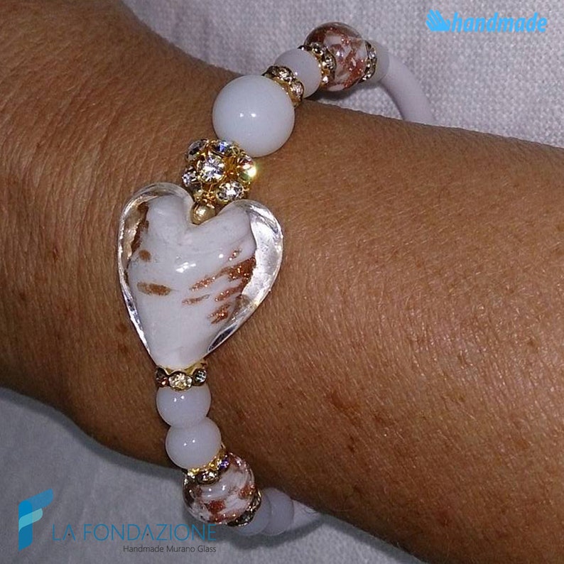 May include: White heart-shaped Murano glass bracelet with gold accents and clear crystal beads. The bracelet is handmade and features a delicate, swirling pattern in the glass.