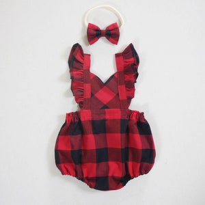 Könnte beinhalten: Rotes und schwarzes kariertes Baby-Overall mit Rüschenträgern und passendem Schleifen-Haarband.