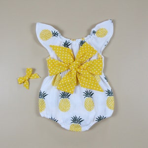May include: White baby romper with yellow pineapple print and a large yellow polka dot bow. A matching yellow bow is also included. The romper has flutter sleeves and is designed for infants.