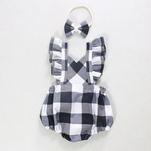 May include: A black and white checkered baby onesie with ruffled sleeves and a criss-cross strap design. A matching black bow headband is included.