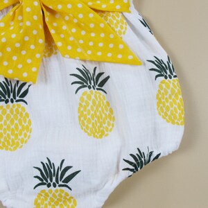 May include: White romper with a yellow pineapple print and a large yellow bow with white polka dots. The romper features a playful design with a tropical theme, perfect for warm weather.