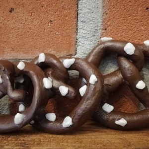 May include: Four chocolate-colored pretzels with white sprinkles. The pretzels are arranged in a row, with the largest pretzel in the back and the smallest pretzel in the front.