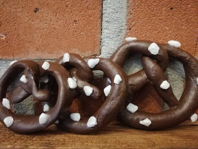 May include: Four chocolate-colored pretzels with white sprinkles. The pretzels are arranged in a row, with the largest pretzel in the back and the smallest pretzel in the front.