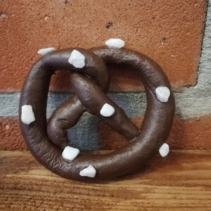 May include: A brown pretzel with white sugar crystals on top. The pretzel is sitting on a wooden surface.
