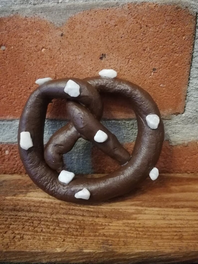 May include: A brown pretzel with white sugar crystals on top. The pretzel is sitting on a wooden surface.