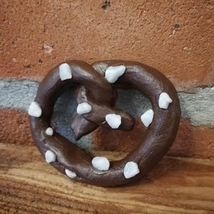 May include: A brown pretzel with white sugar crystals on top. The pretzel is on a wooden surface.